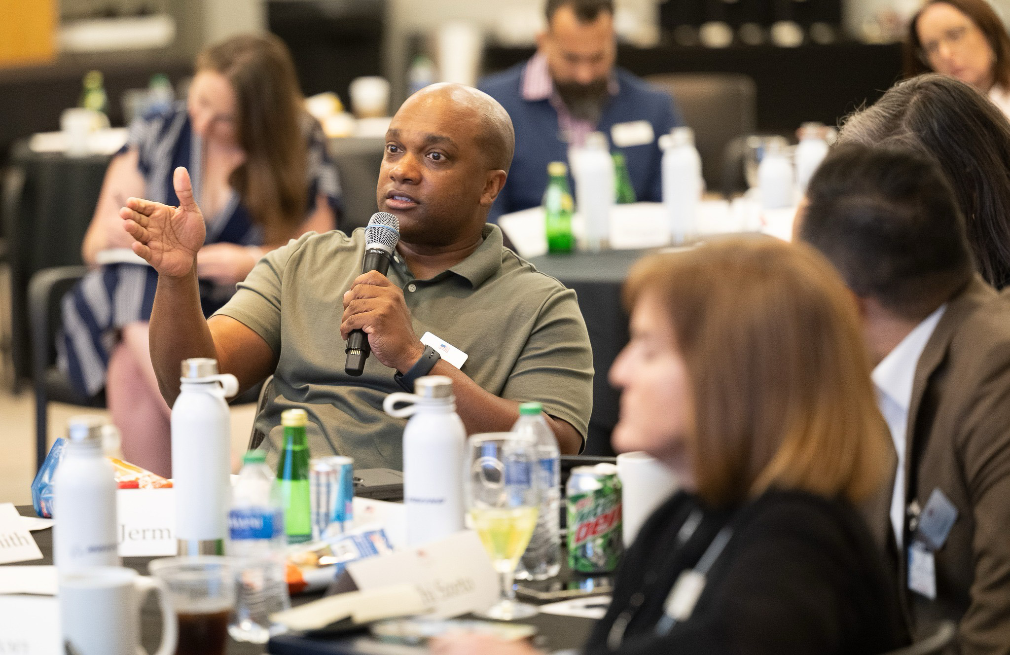 man speaking at conference at a table using a handheld mic